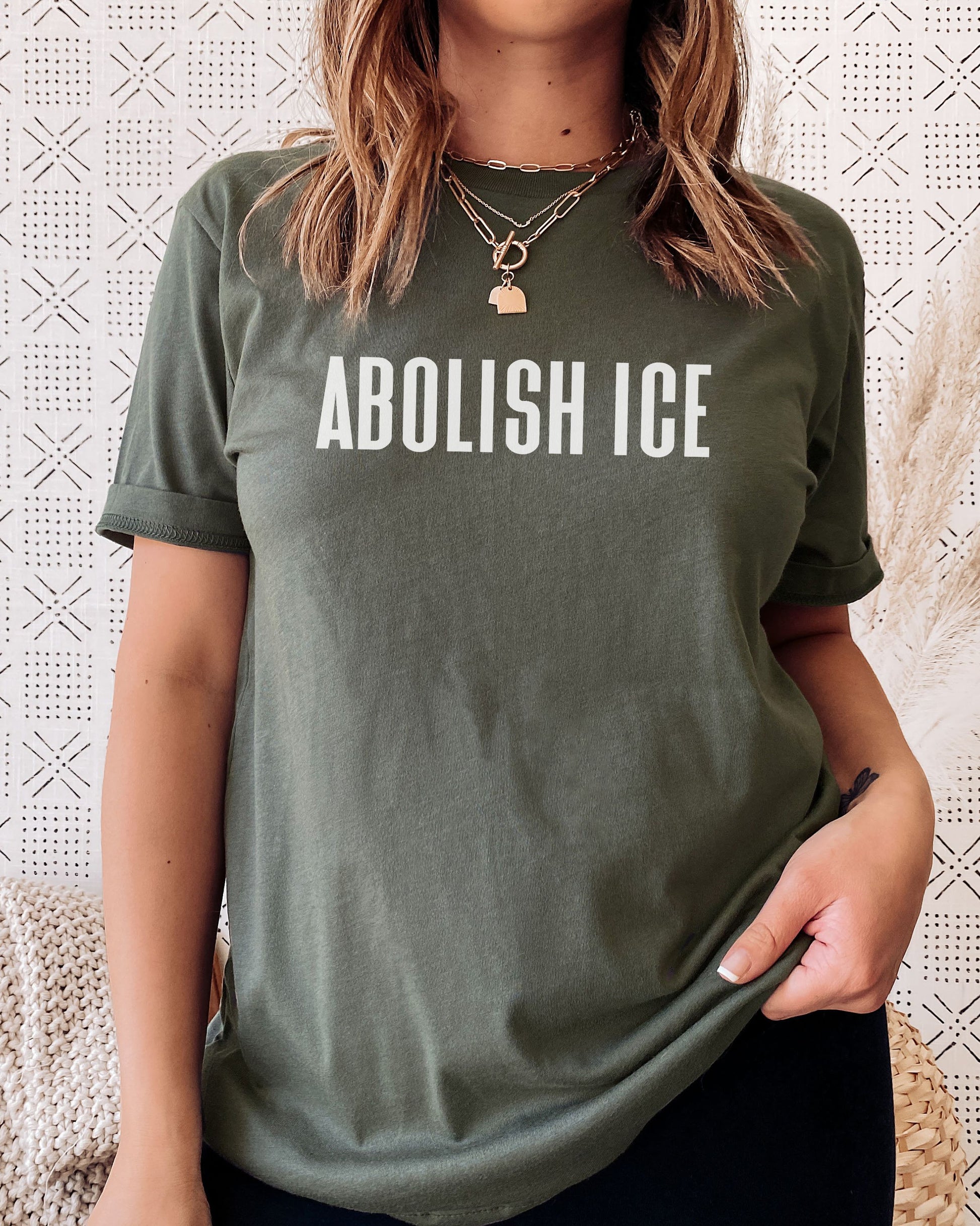 Person wearing a green t-shirt with 'ABOLISH ICE' text against a textured white background