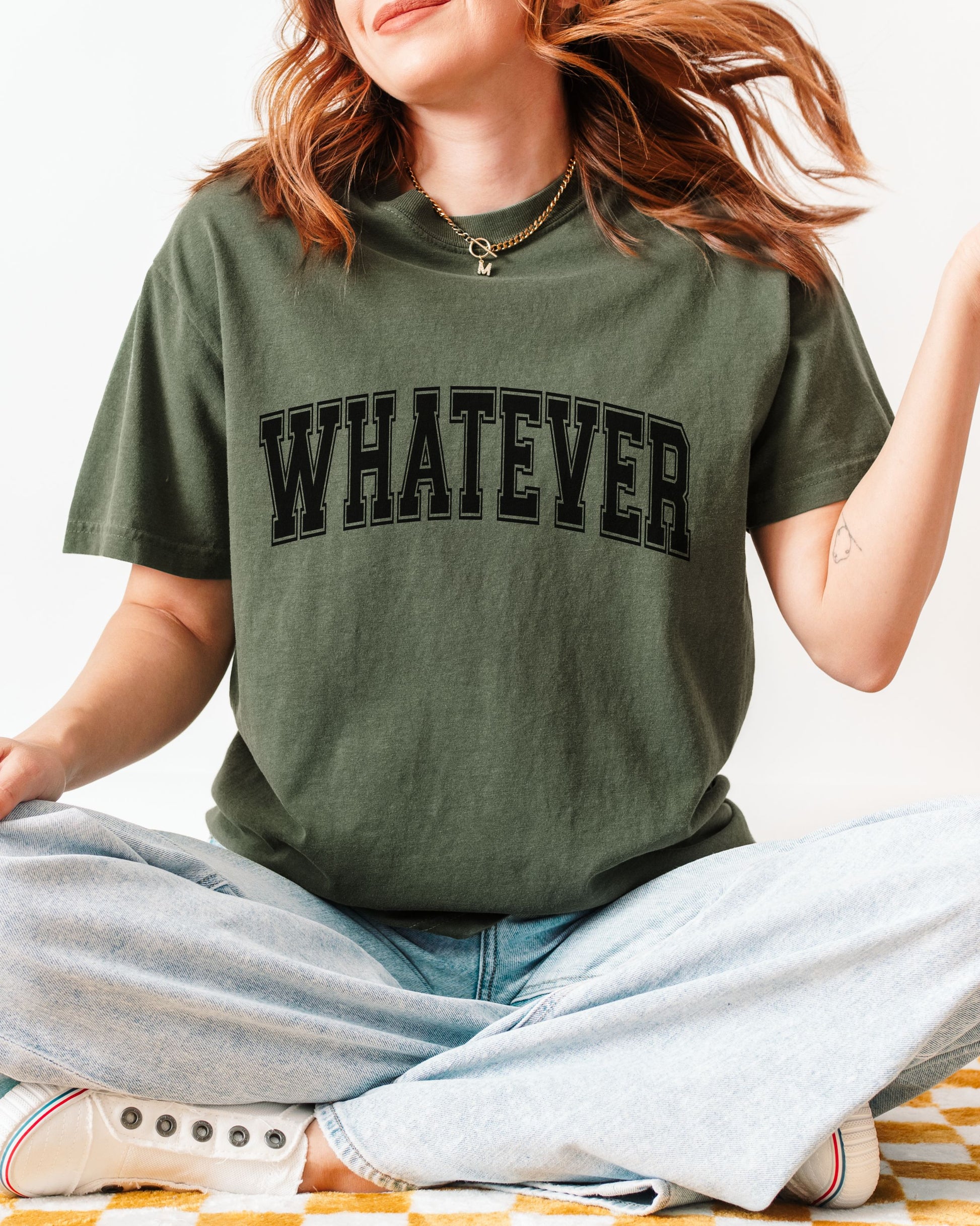 Person wearing a green t-shirt with 'WHATEVER' text, sitting on a striped surface.