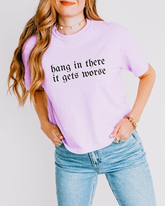 Person wearing a light purple t-shirt with text and blue jeans on a plain background
