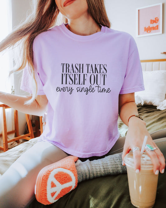 Person wearing a purple t-shirt with text, sitting on a couch holding a drink.
