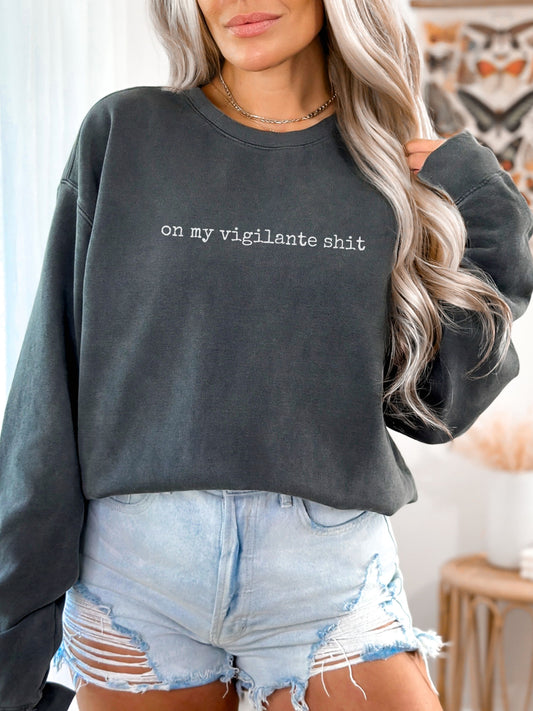 Person wearing a dark gray sweatshirt with text and denim shorts indoors.