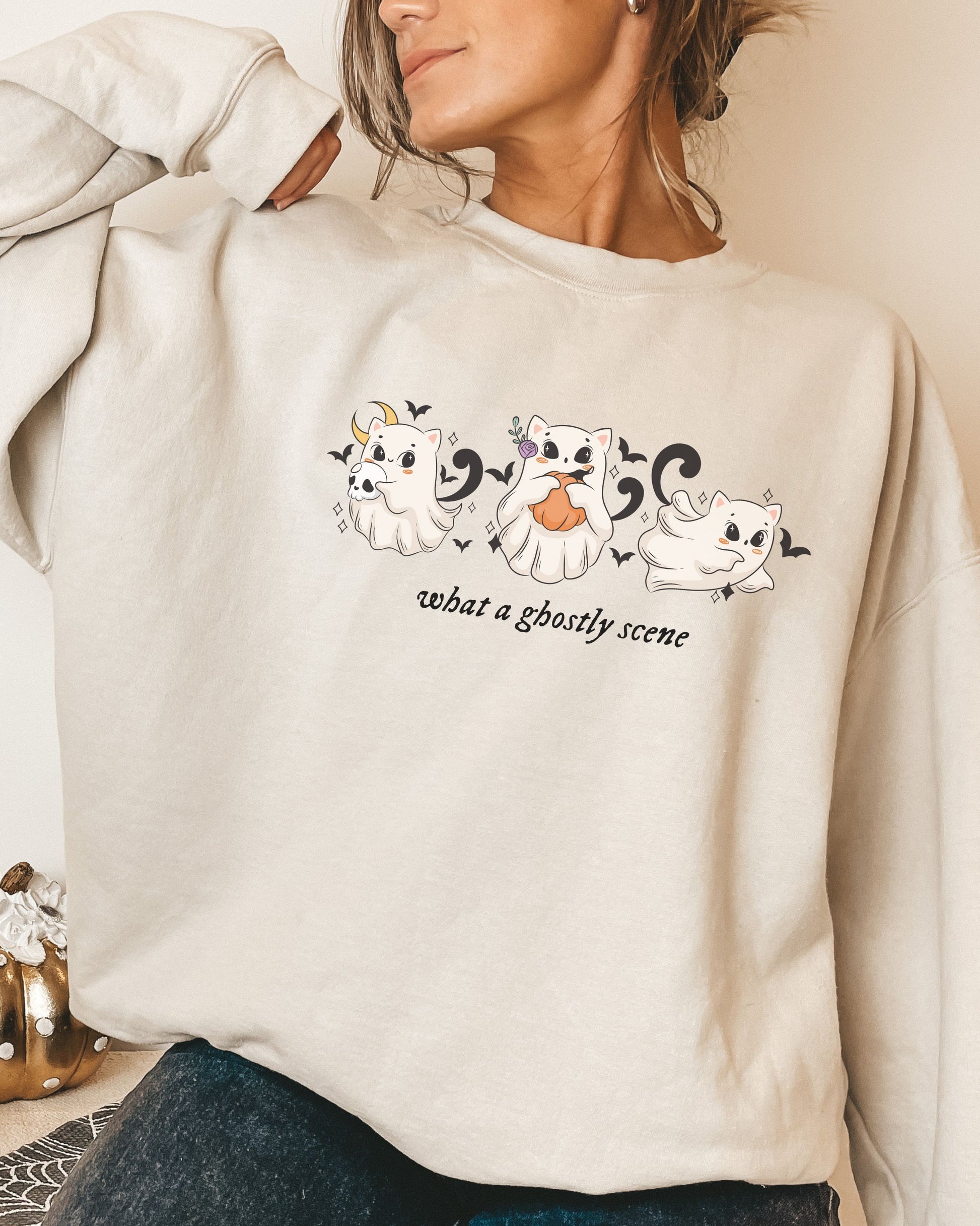 Beige sweatshirt with ghost illustrations and text worn by a person