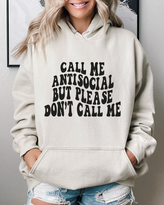 Person wearing a beige hoodie with text 'Call me antisocial but please don't call me' in a casual setting.