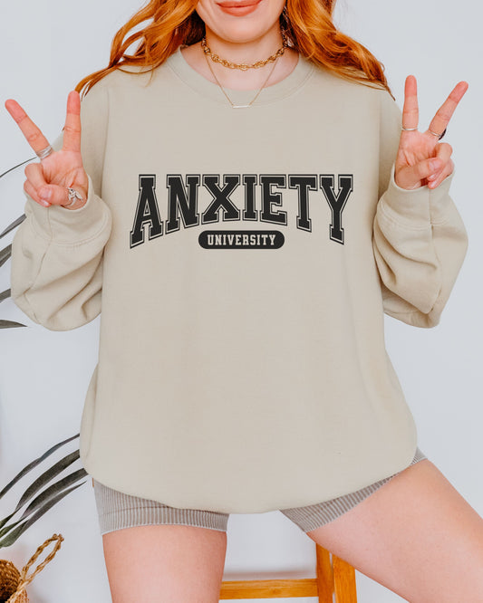 Person wearing a beige sweatshirt with 'ANXIETY UNIVERSITY' text, making peace signs.