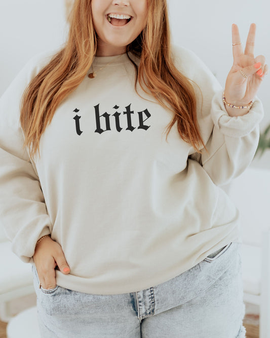 Person wearing a beige sweatshirt with 'i bite' text, making a peace sign.