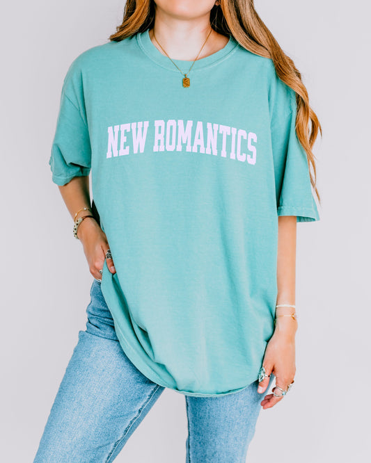 Person wearing a teal t-shirt with 'NEW ROMANTICS' text on a plain background