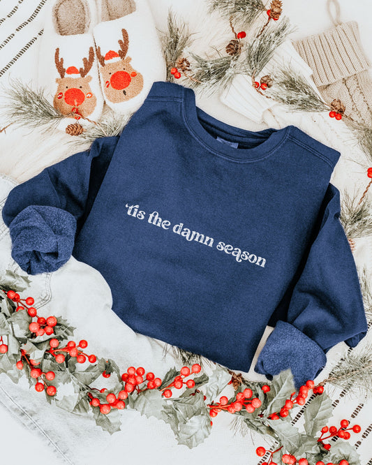 Navy blue sweatshirt with 'tis the damn season text on a festive background with holly and reindeer.