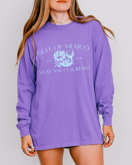 Purple long-sleeve shirt with graphic design and text worn by a person on a plain background