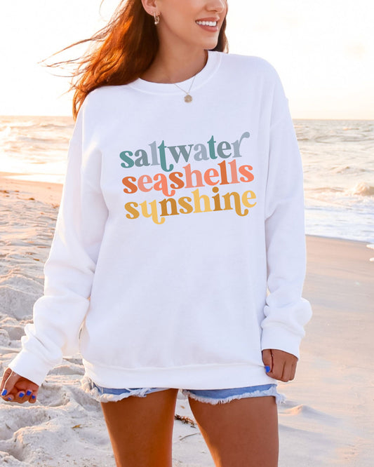 Person wearing a white sweatshirt with colorful text on a beach