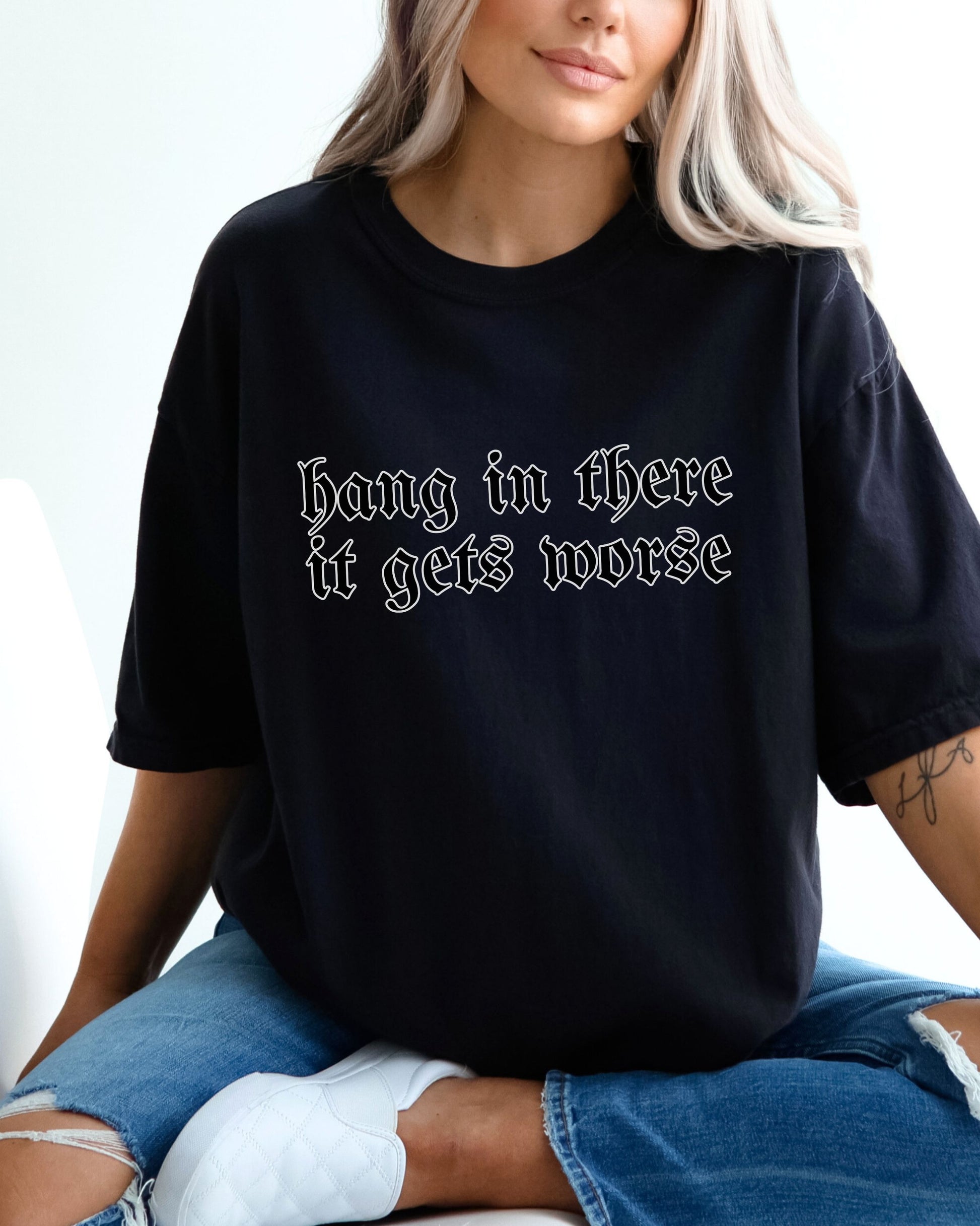 Person wearing a black t-shirt with text 'Hang in there it gets worse' on a plain background