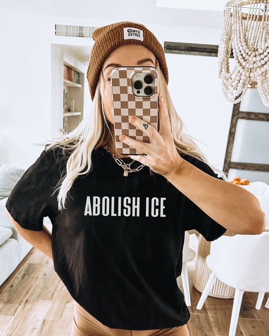 Person wearing a black t-shirt with 'ABOLISH ICE' text, taking a mirror selfie.