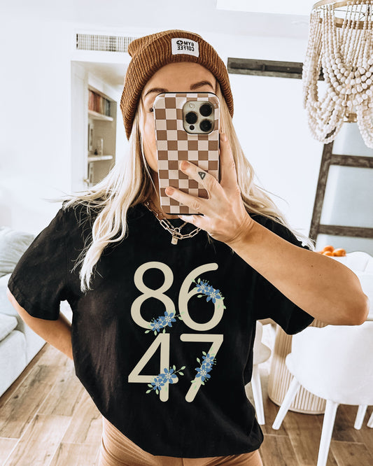 Person wearing a black t-shirt with '8647' design, taking a mirror selfie.