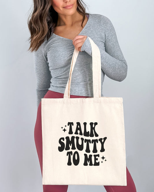Person holding a tote bag with 'Talk Smutty to Me' text against a plain background