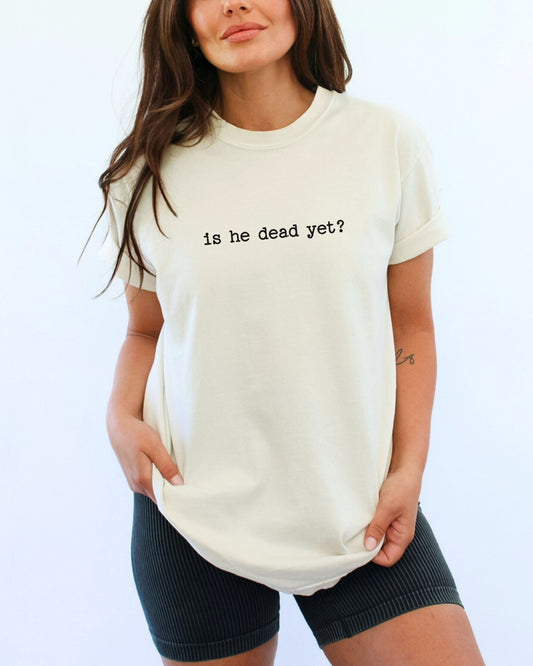 Woman wearing an ivory t-shirt with 'is he dead yet?' text on a plain background