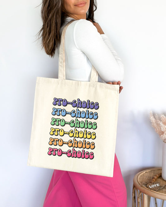 Person holding a tote bag with 'pro-choice' text in colorful letters against a white background