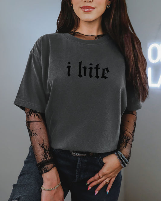 Person wearing a gray t-shirt with 'i bite' text, standing against a neutral background.