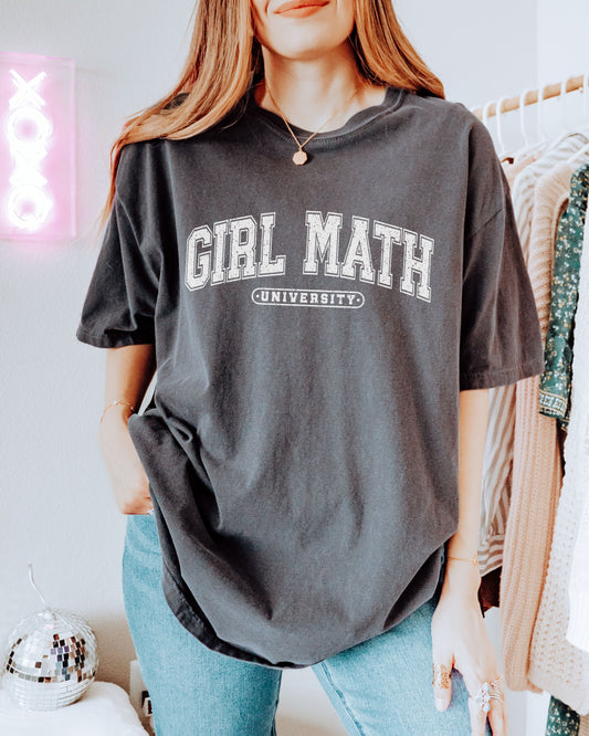 Person wearing a dark gray t-shirt with 'GIRL MATH UNIVERSITY' text in a casual setting.