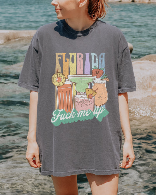 Person wearing a gray t-shirt with a colorful 'Florida' graphic design by a body of water.