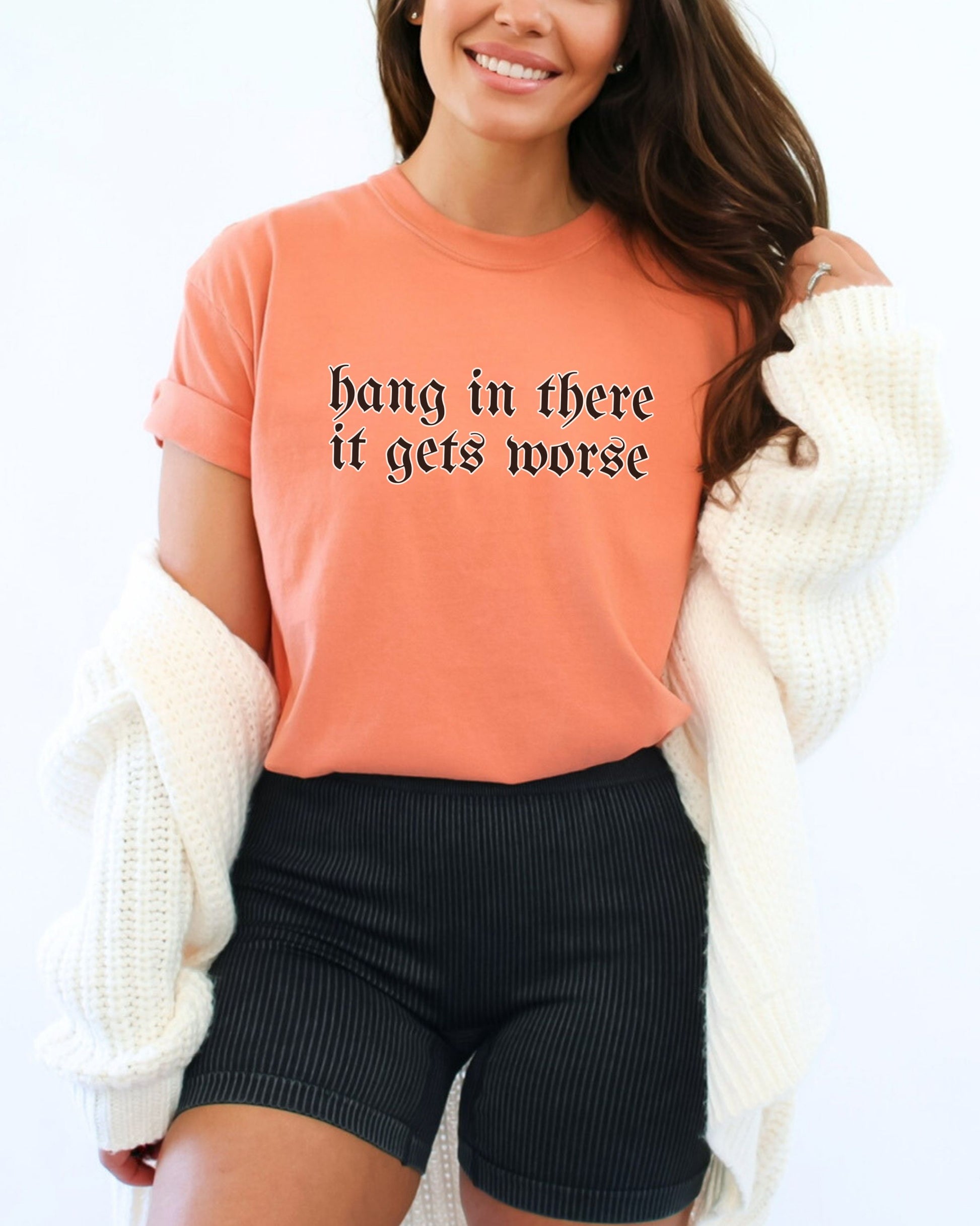 Woman wearing an orange shirt with text and black shorts, smiling.